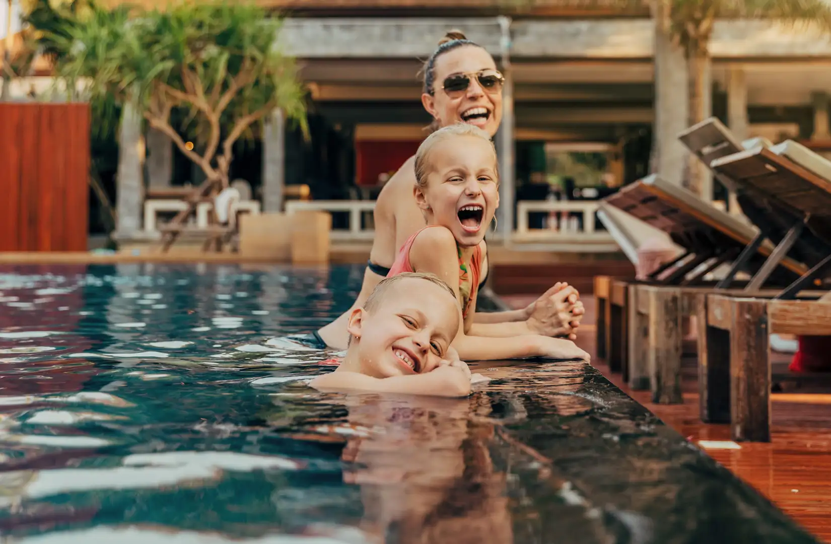 Mutter mit zwei Kindern im Pool die in die Kamera lächeln und eine gute Zeit im Urlaub haben