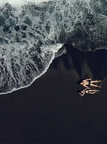 Eltern mit Kind Eltern halten ihre Tochter an den Händen und laufen am Strand aus dem Meerwasser heraus.