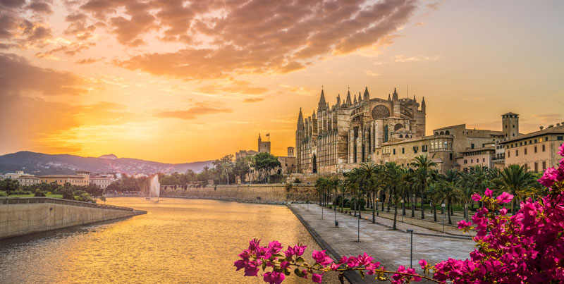 Die Kathedrale von Palma de Mallorca bei Sonnenuntergang, der sie Szene in ein sanftes oranges Licht einhüllt.