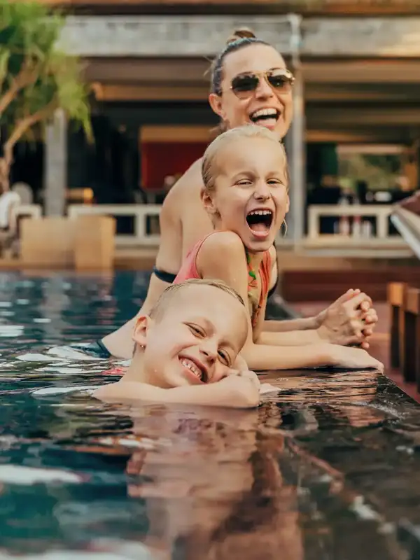 Mutter mit zwei Kindern im Pool die in die Kamera lächeln und eine gute Zeit im Urlaub haben