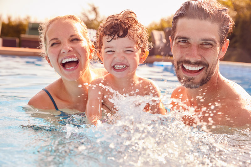 Glückliche, freudig strahlende Familie mit ihrem rothaarigen Jungen im Hotelpool.