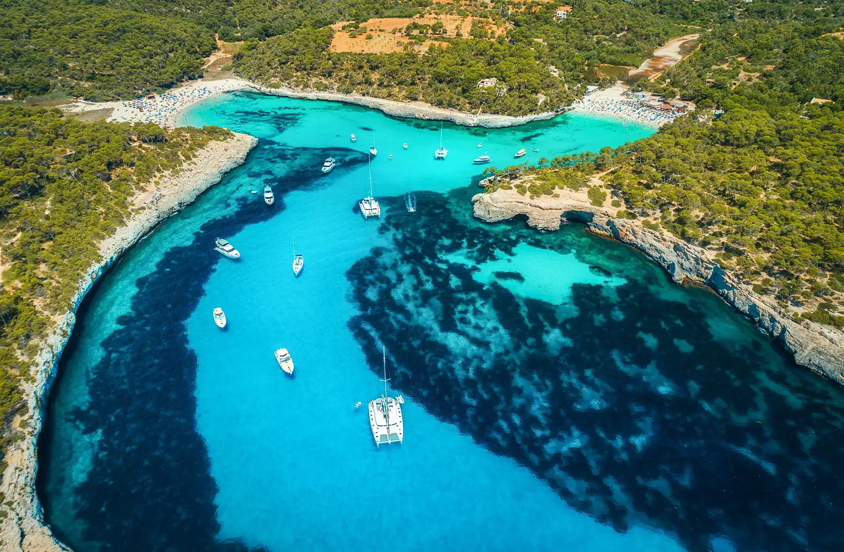 Luftaufnahme von einer Badebucht mit Booten und transparentem Meer an sonnigen Tage auf Mallorca