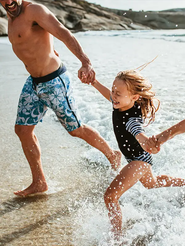 Kind mit Eltern Eltern halten ihre Tochter an den Händen und laufen am Strand aus dem Meerwasser heraus.