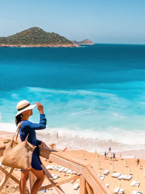 Junge Frau mit Hut im blauen Kleid auf Anhöhe blickt an einem schönen Sommertag auf den Strand von Kaputas herab.